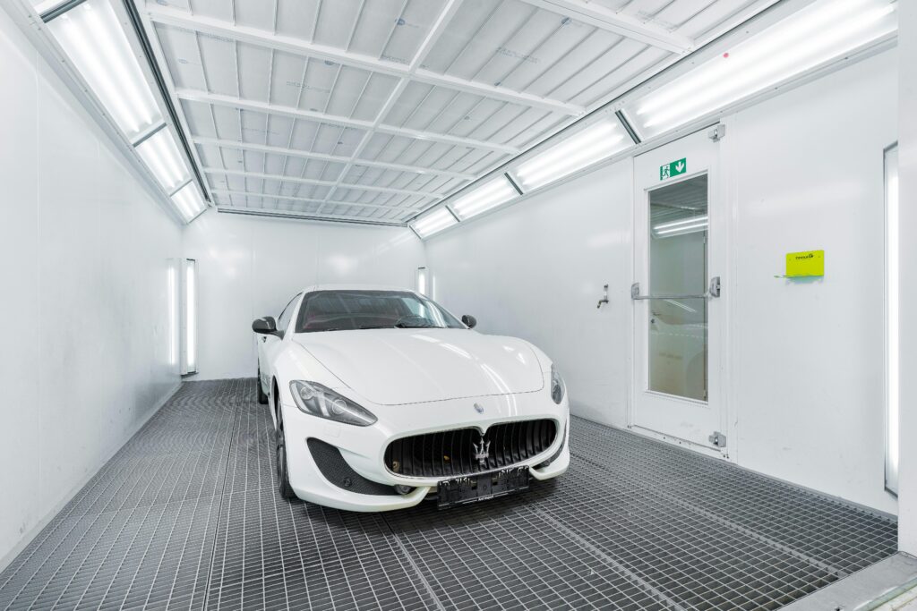 White luxury car inside a well-lit paint booth, showcasing sleek design and sophistication.